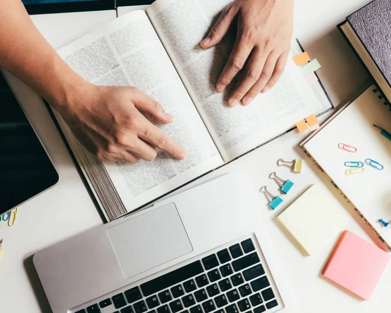 Student studying with open books, a laptop, and stationery supplies on a desk, representing preparation and academic assessment.