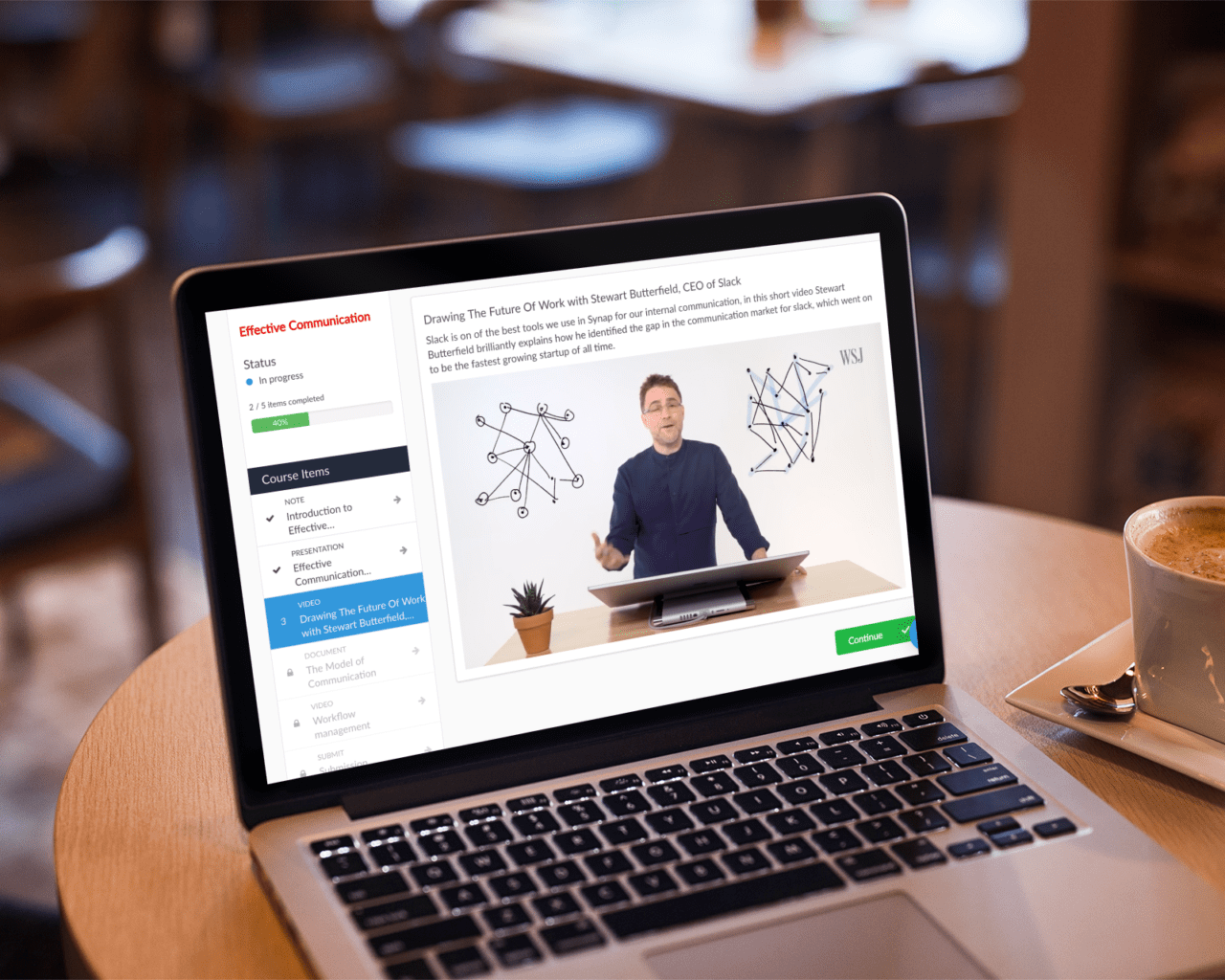 Online course video on Synap platform displayed on MacBook on coffee table