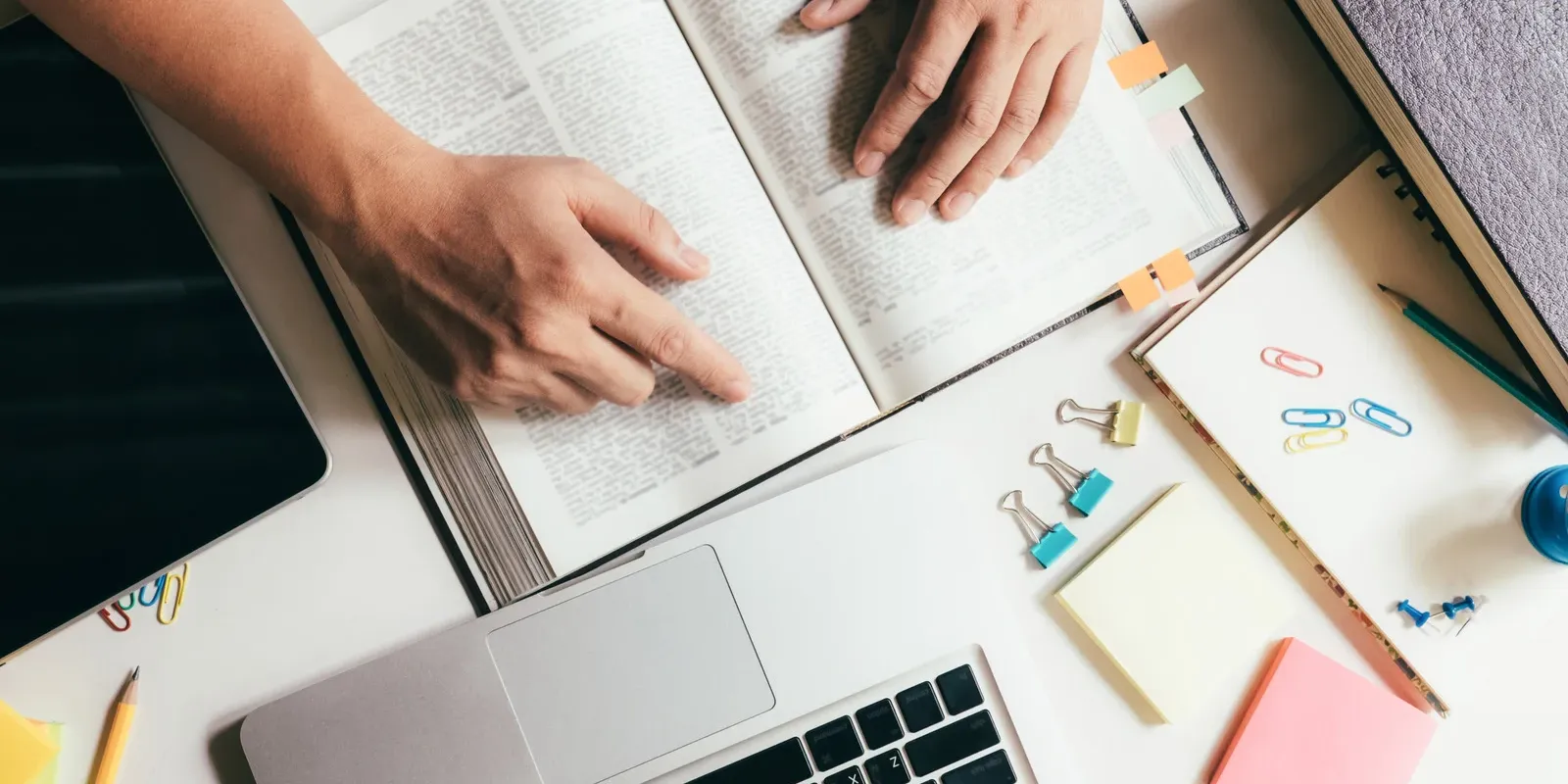 Student studying with open books, a laptop, and stationery supplies on a desk, representing preparation and academic assessment.