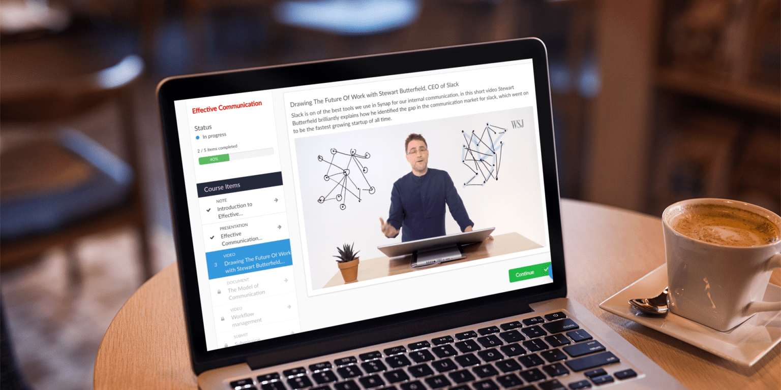 Online course video on Synap platform displayed on MacBook on coffee table