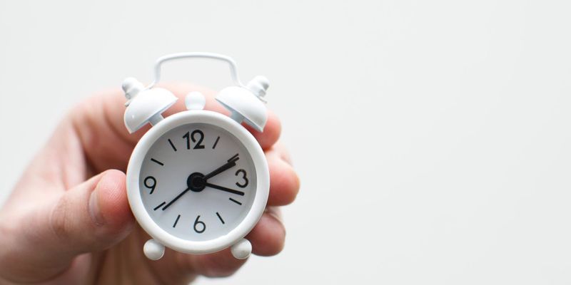 A person holding a small alarm clock.