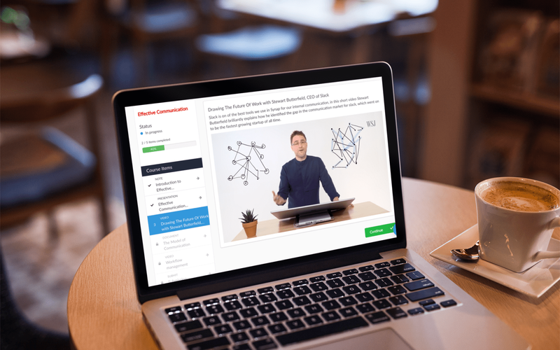 Online course video on Synap platform displayed on MacBook on coffee table