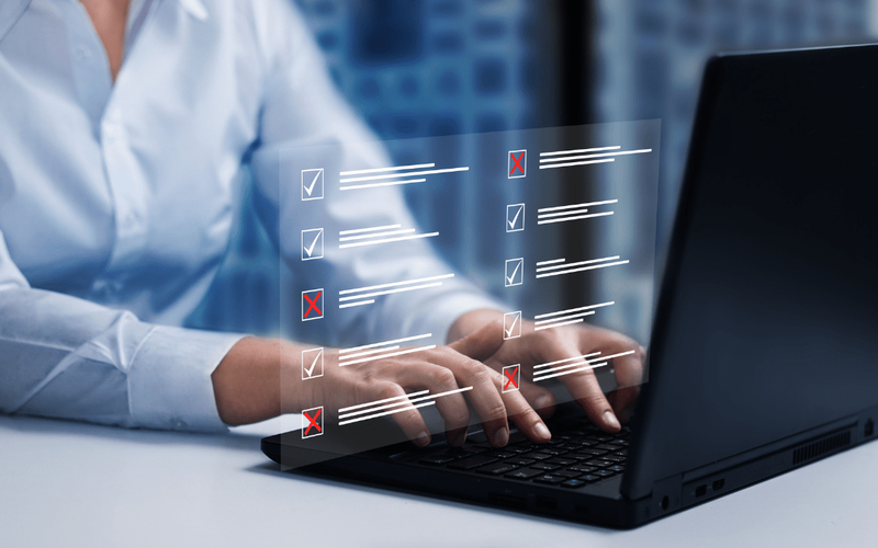 Hands typing on a laptop with a digital checklist overlay representing online exam marking and automated assessment tools.