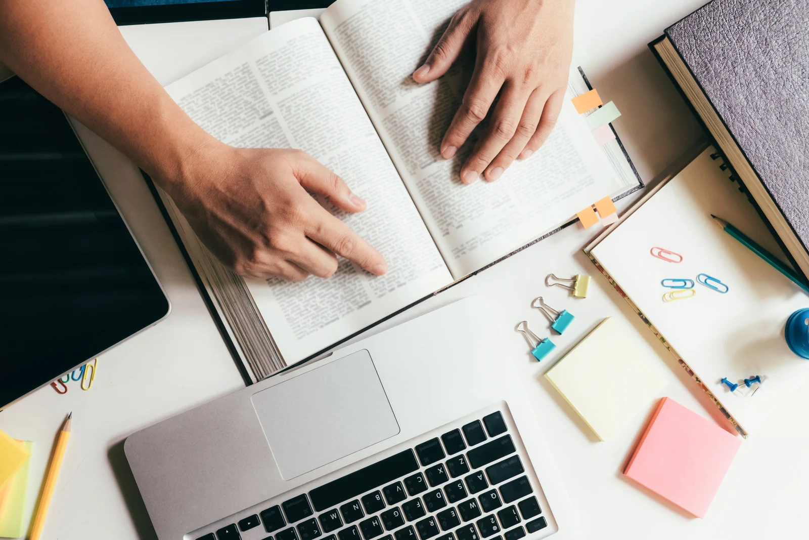 Student studying with open books, a laptop, and stationery supplies on a desk, representing preparation and academic assessment.